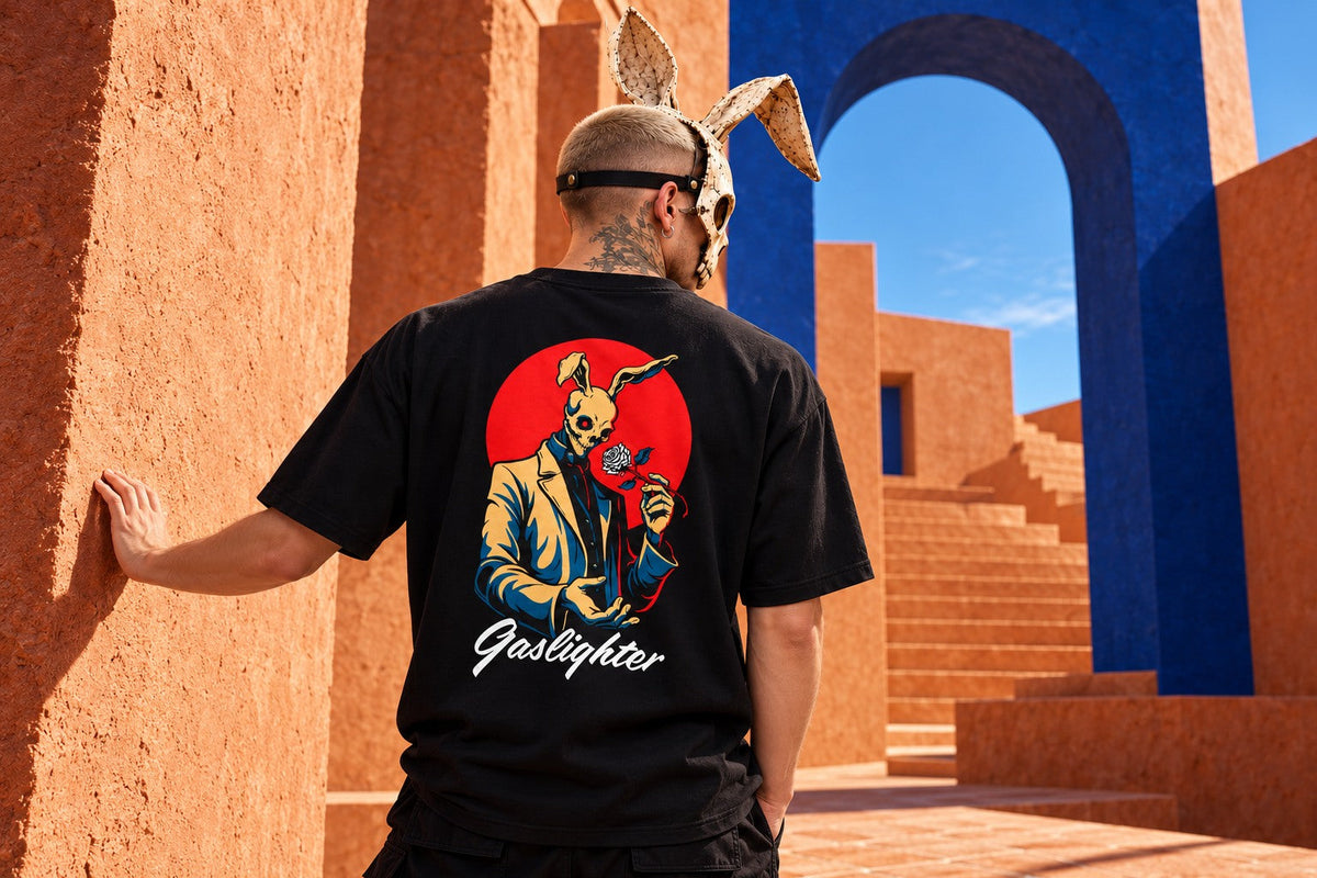 James in a rabbit mask wearing the Gaslighter T-shirt, resting his hand on a sunlit terracotta wall beside a cobalt arch and staircase.