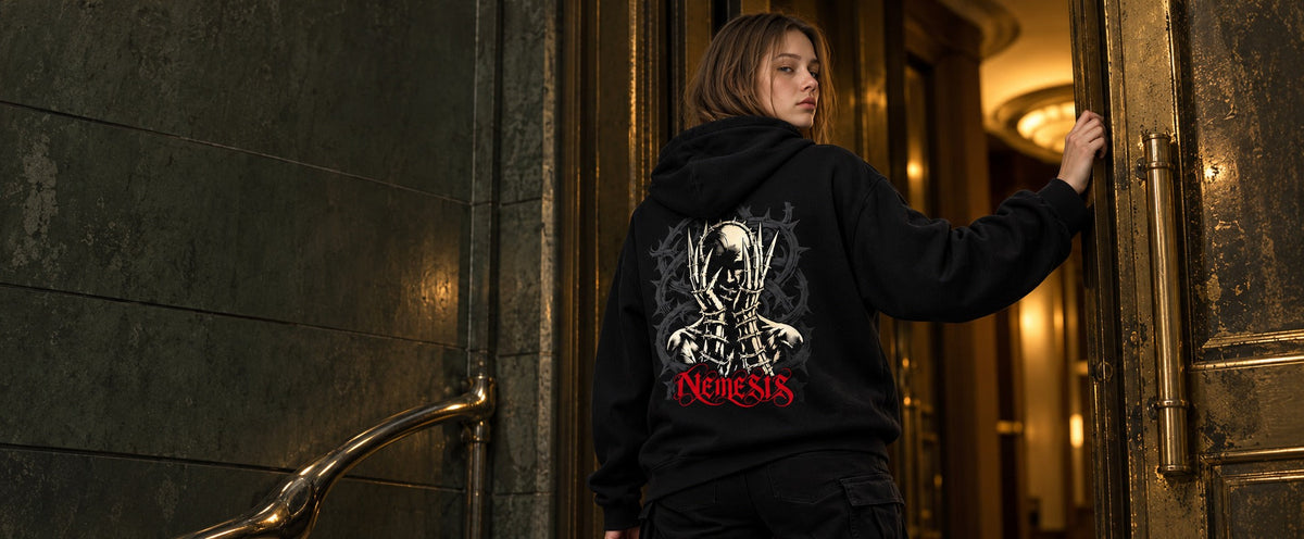 Mara wearing the black Nemesis hoodie, back artwork visible beside an aged brass entrance.