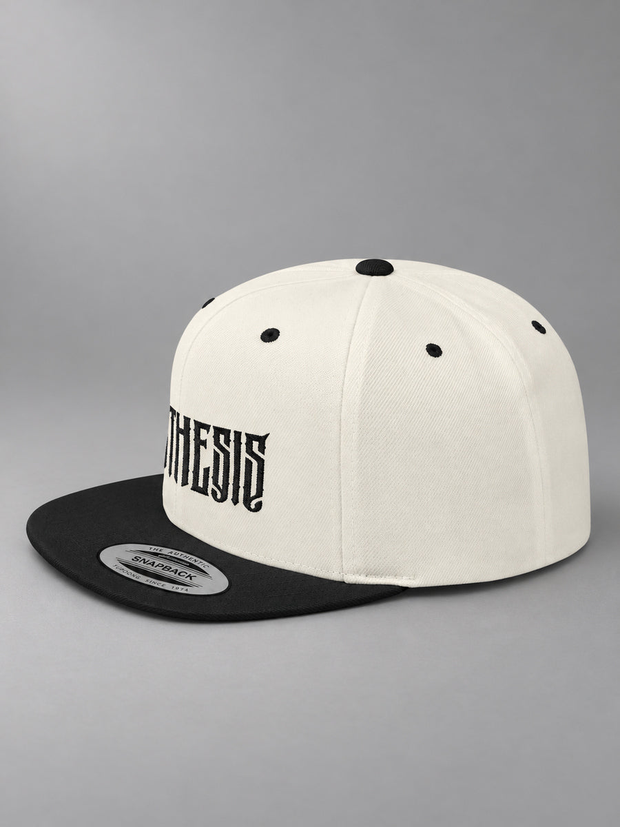 Synthesis Blackout snapback in Natural/Black, three-quarter view showing angular black Synthesis embroidery and flat bill on gray.
