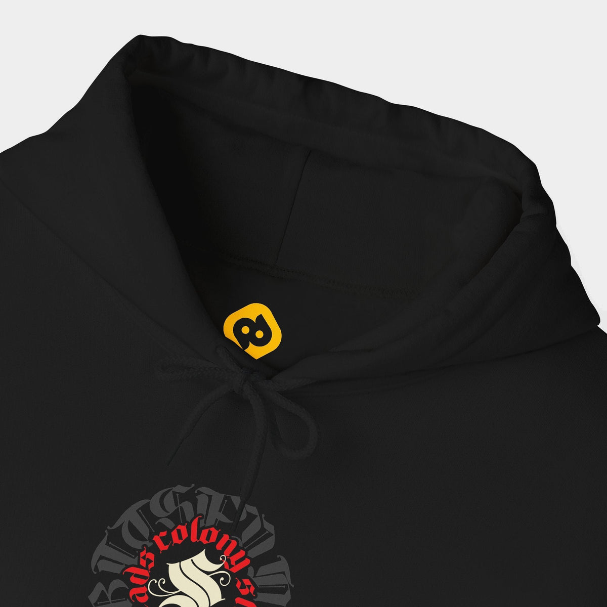 Shroomhead black hoodie neckline and chest close-up showing a round Colony Shroomheads crest in red and ivory over charcoal lettering.