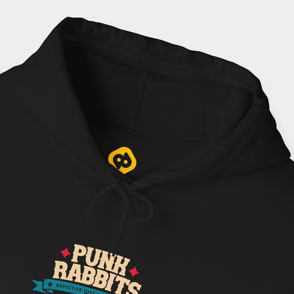 Cannibal Ted black hoodie neckline and chest close-up showing compact cream PUNK RABBITS lettering with red stars, a teal Defective Toys Collection banner and red ornament and yellow neck branding.