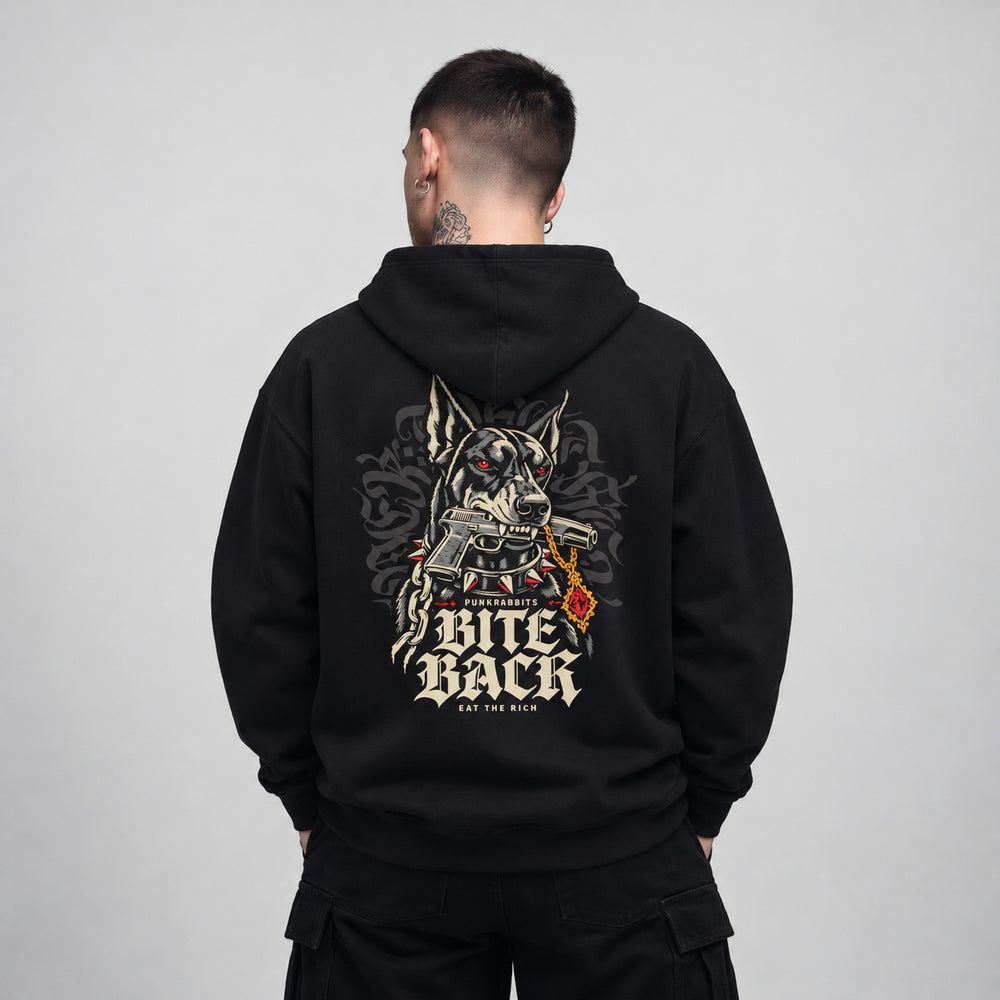 Nico wearing the black Bite Back hoodie, back view showing a Doberman with red eyes and a spiked collar, gripping an illustrated handgun, beside a gold chain and red pendant; Punkrabbits, Bite Back and Eat the Rich lettering complete the composition.