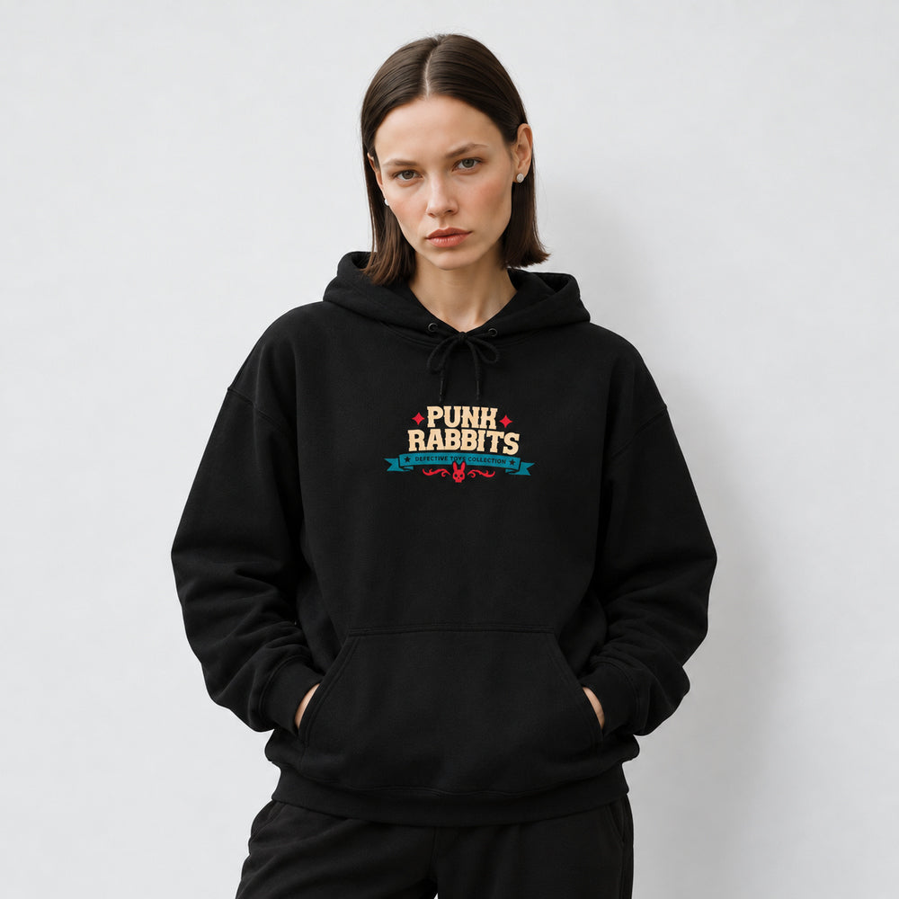 Mara wearing the black Cannibal Ted hoodie, front view showing compact cream PUNK RABBITS lettering with red stars, a teal Defective Toys Collection banner and red ornament.