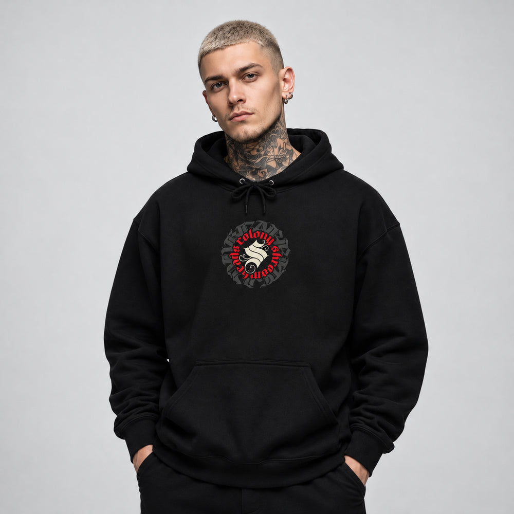 James wearing the black Colony hoodie, front view showing a circular Colony Shroomheads crest in ivory and red over charcoal lettering.