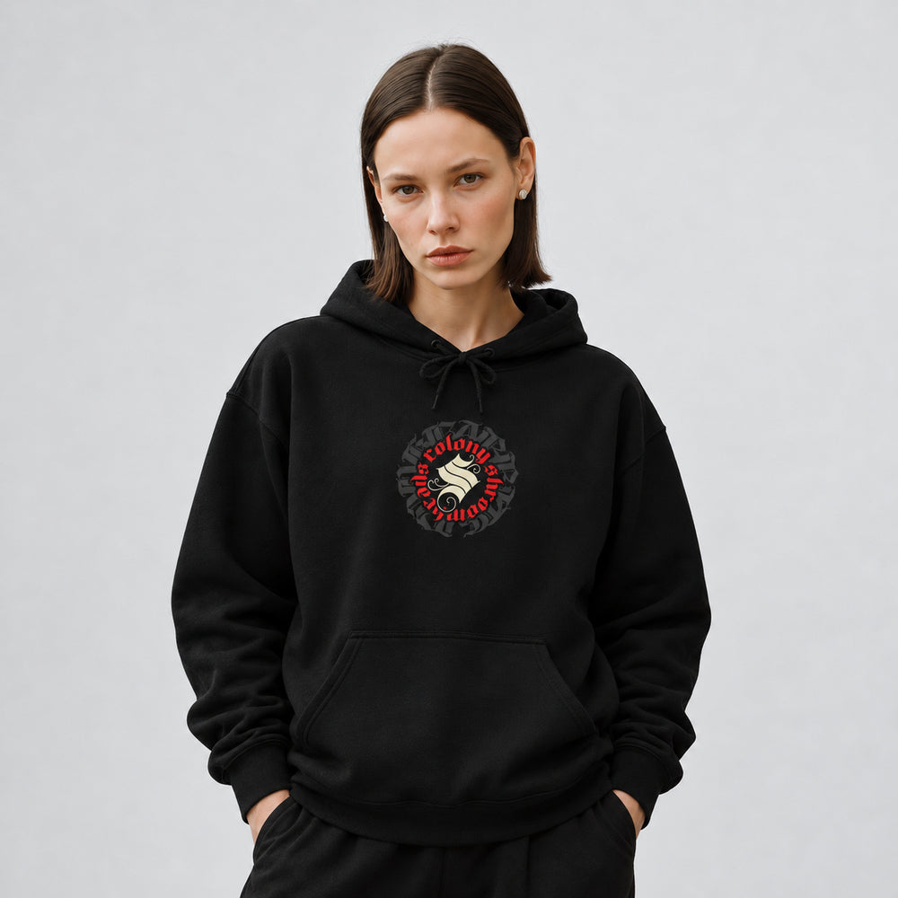 Mara wearing the black Colony hoodie, front view showing a circular Colony Shroomheads crest in ivory and red over charcoal lettering.
