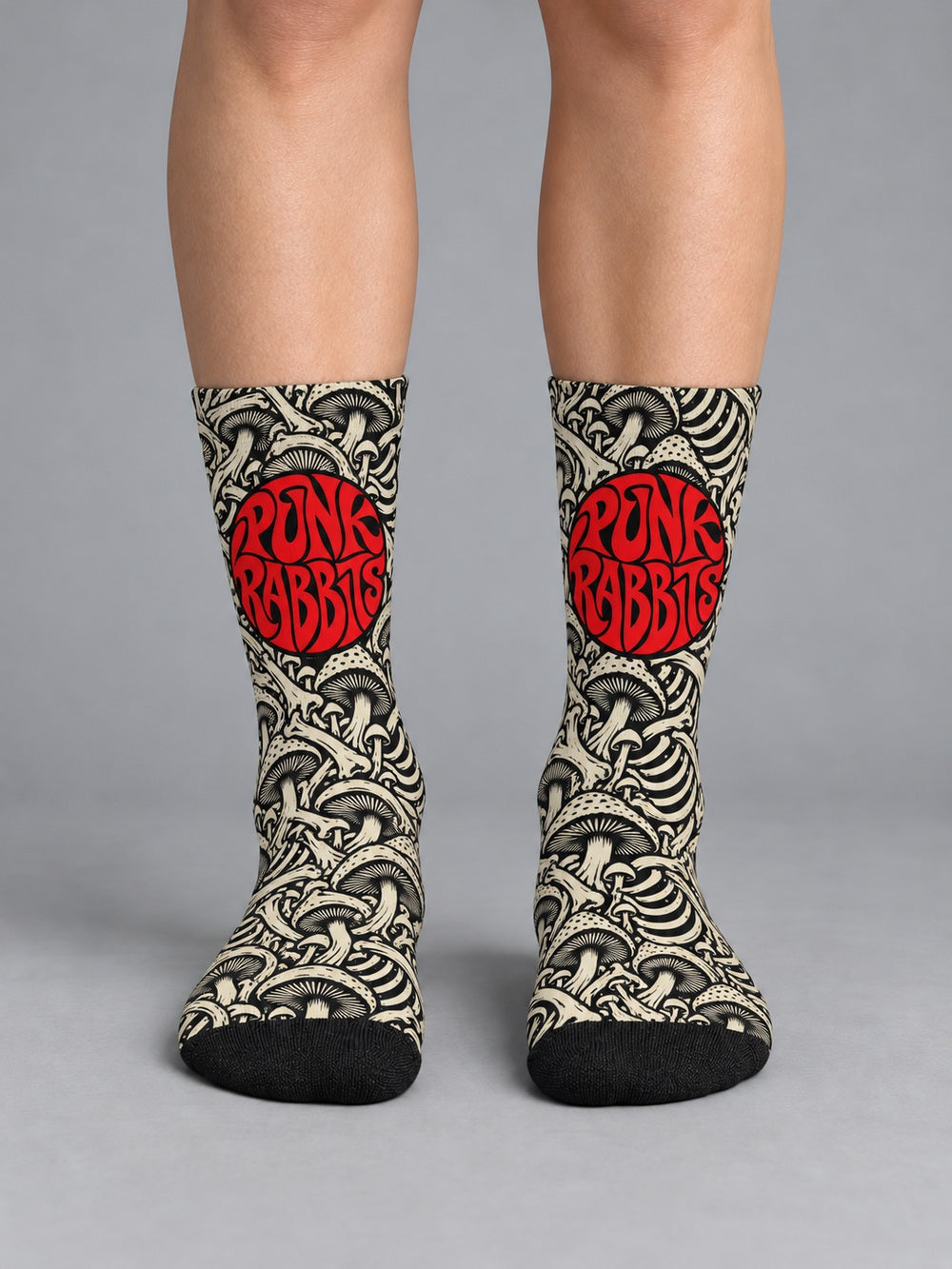 Front view worn on lower legs without shoes: black crew socks with ivory mushroom and skeletal artwork and a red circular Punkrabbits logo.