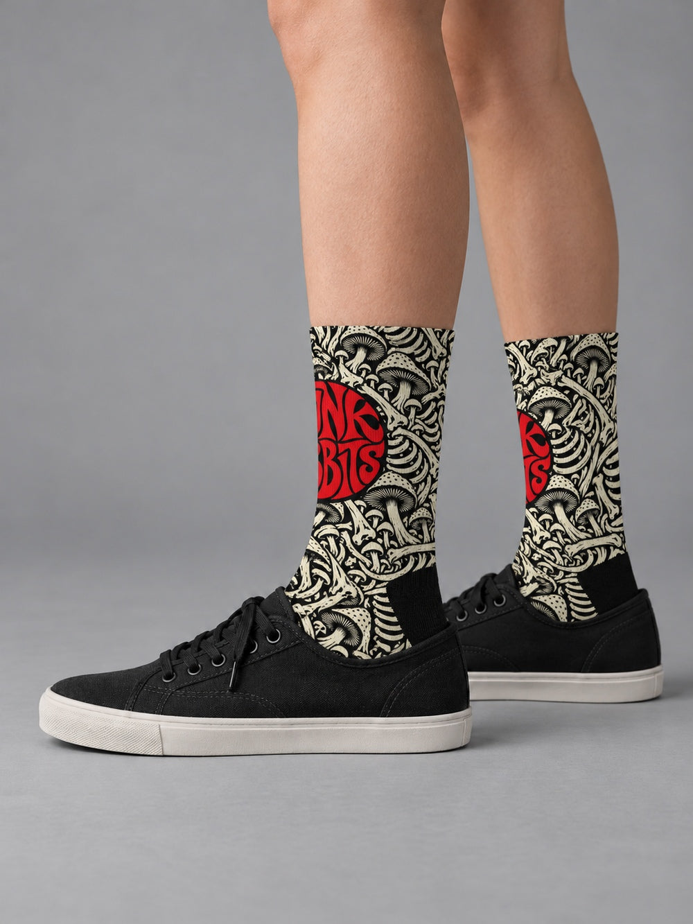 Side view worn with black low-top canvas shoes: black crew socks with ivory mushroom and skeletal artwork and a red circular Punkrabbits logo.