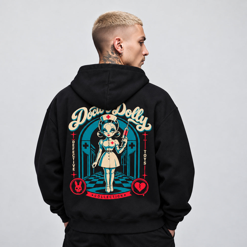 James wearing the black Doctor Dolly hoodie, back view showing a cracked porcelain nurse doll holding a red syringe in a teal hospital corridor, beneath cream Doctor Dolly lettering, with red rabbit and broken-heart emblems.