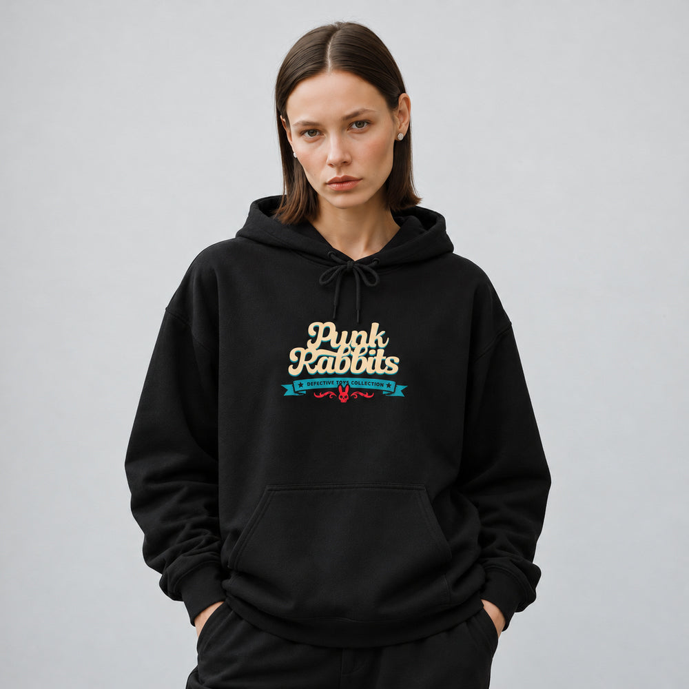 Mara wearing the black Doctor Dolly hoodie, front view showing cream Punk Rabbits script above a teal banner and small red ornament.