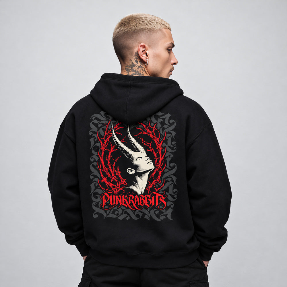 James wearing the black Ecstasis hoodie, back view showing an ivory upward-tilted horned portrait framed by red branching thorns and charcoal ornament, with red Punkrabbits lettering.