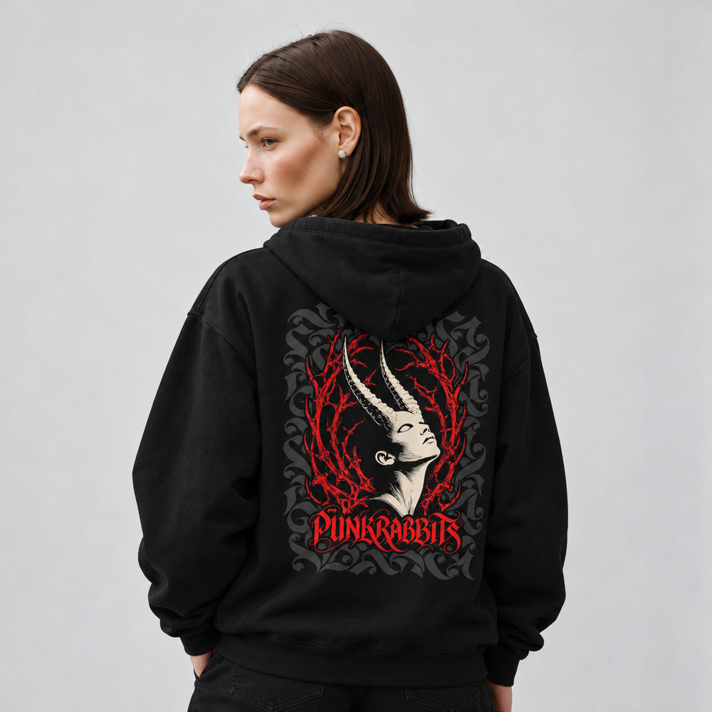 Mara wearing the black Ecstasis hoodie, back view showing an ivory upward-tilted horned portrait framed by red branching thorns and charcoal ornament, with red Punkrabbits lettering.