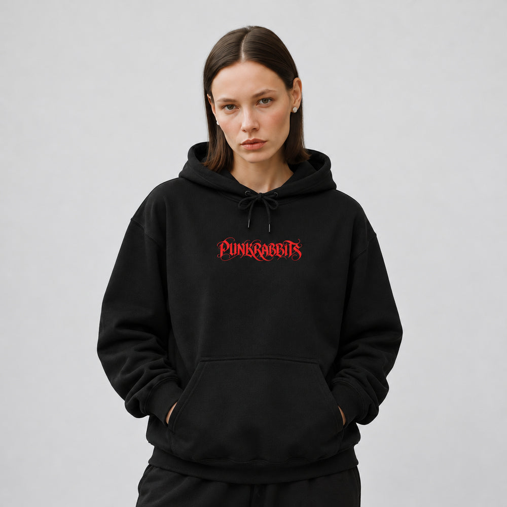 Mara wearing the black Ecstasis hoodie, front view showing a compact red Punkrabbits calligraphic wordmark.