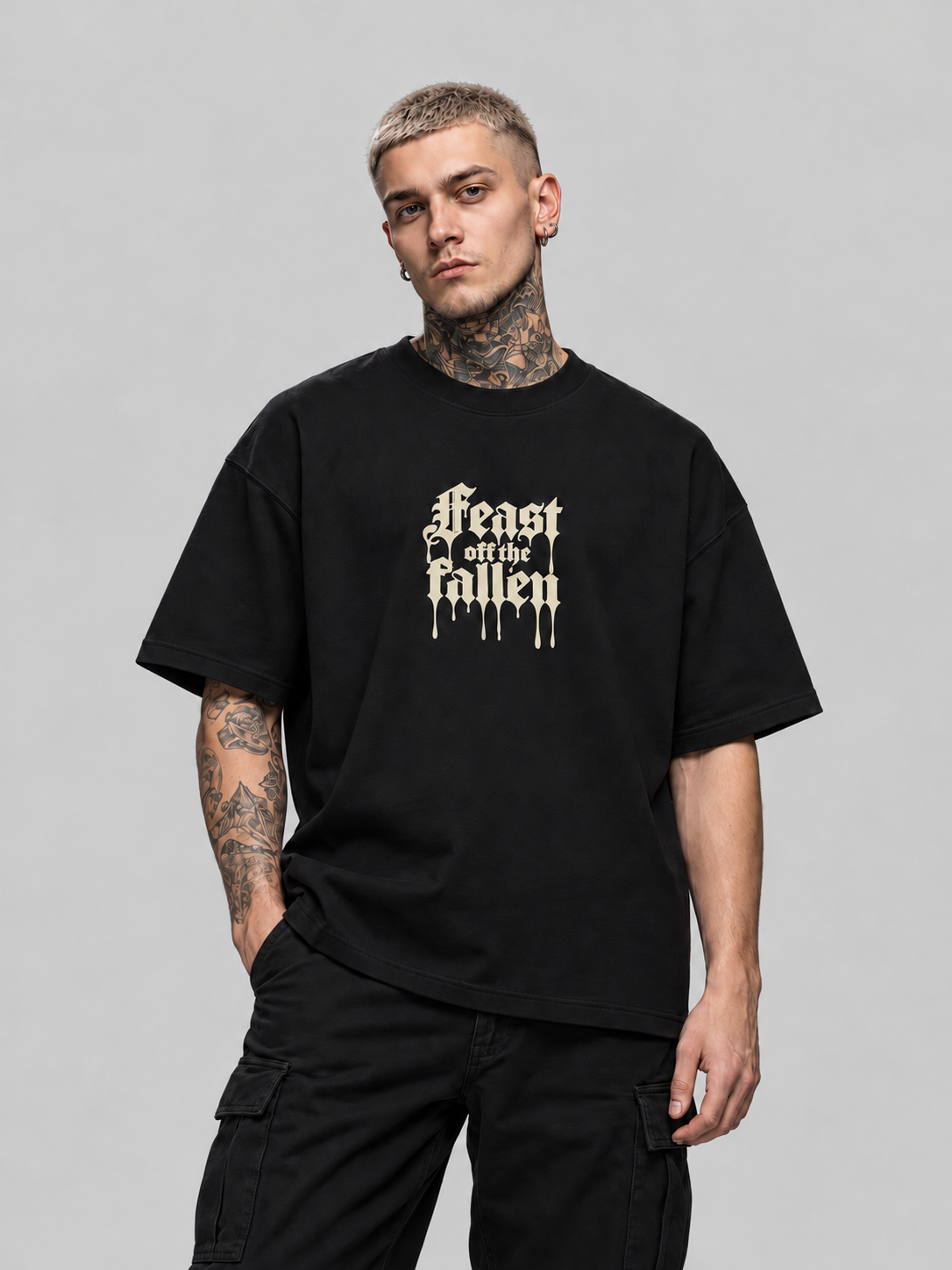 James wearing black Feast off the fallen Premium Boxy Tee, front view with ivory dripping blackletter in a gray studio.