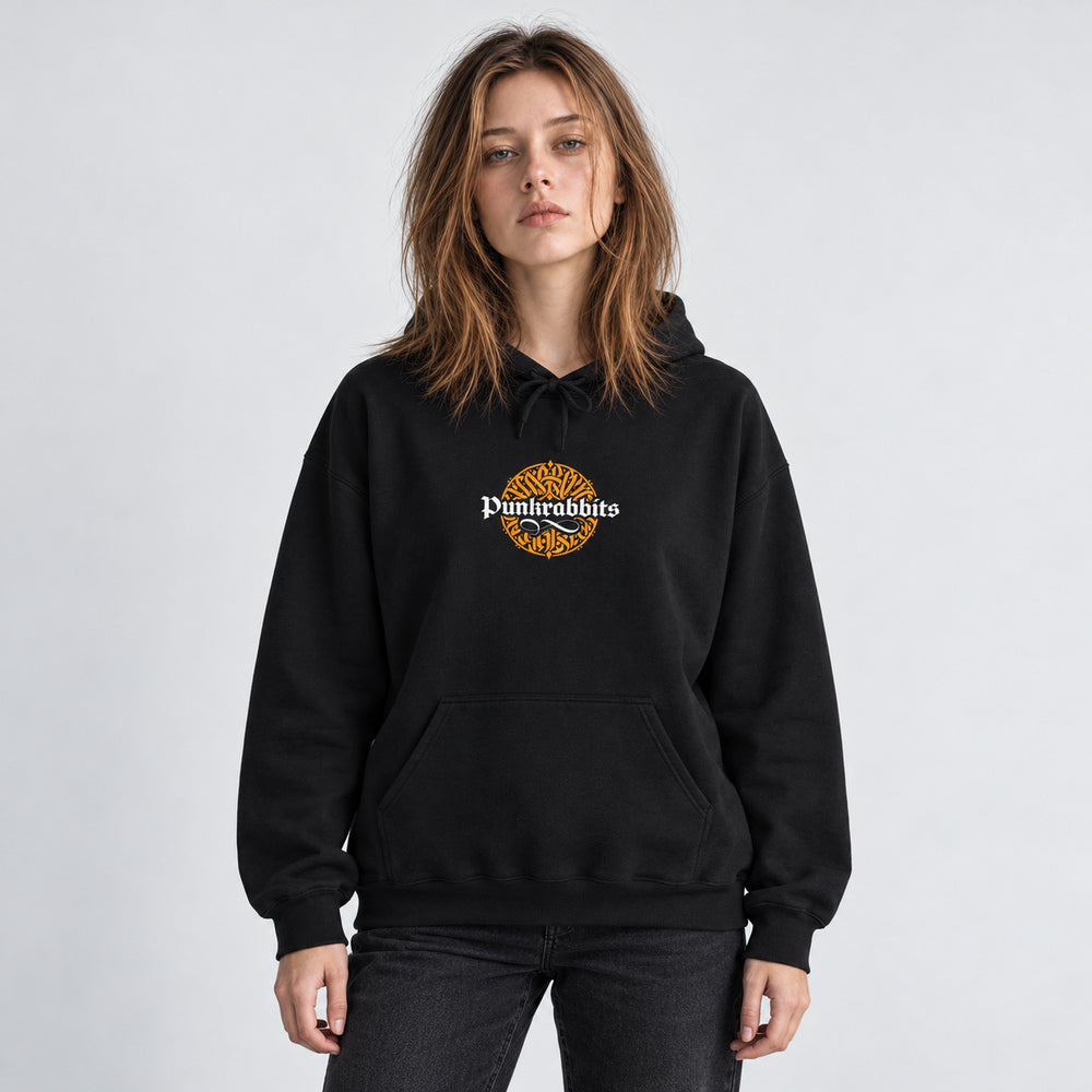 Mara wearing the black Gilded Thrones Turn to Bones hoodie, front view in a pale gray studio.