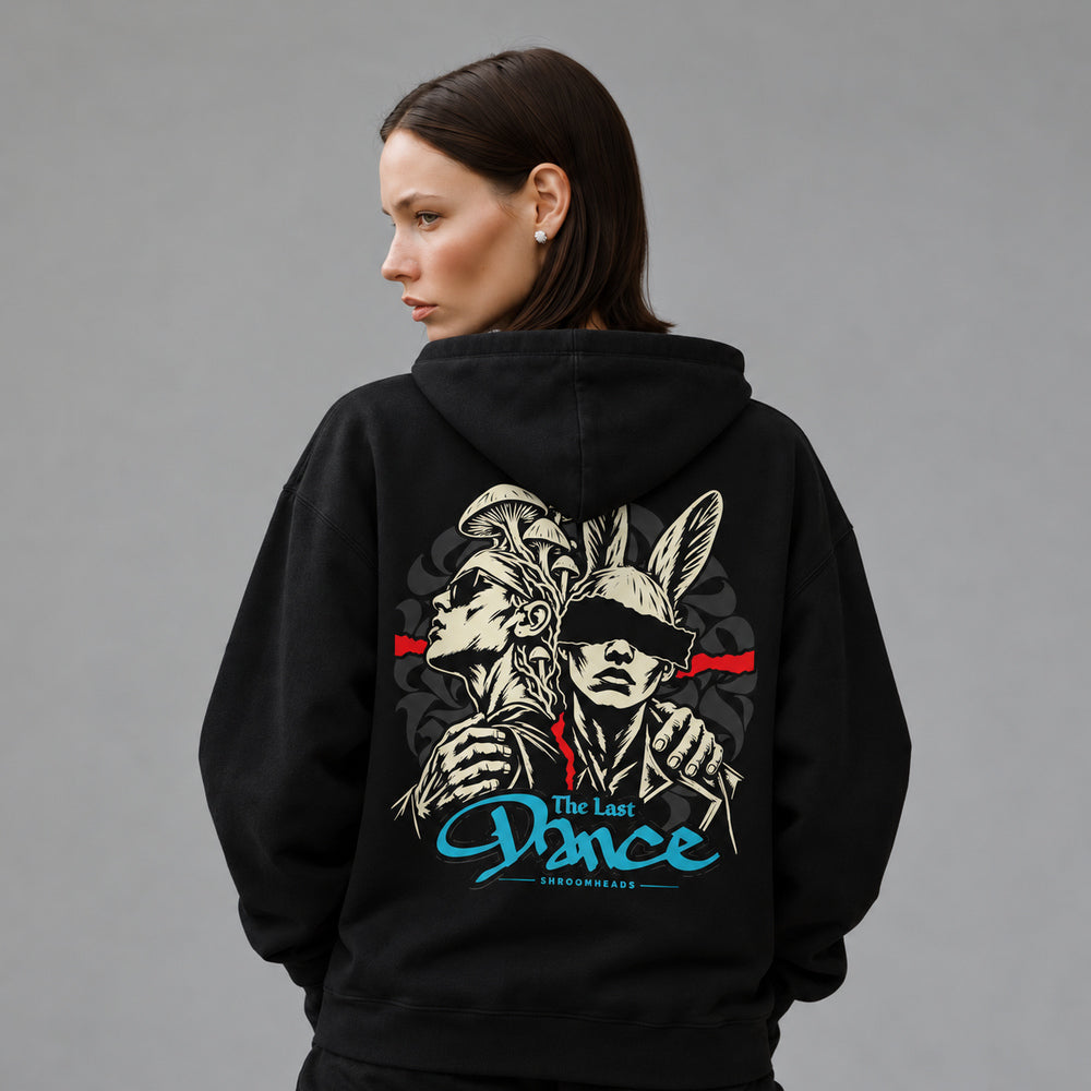 Mara wearing the black Last Dance hoodie, back view showing two linked figures, one mushroom-crowned and one rabbit-eared, with a red band and blue The Last Dance script.
