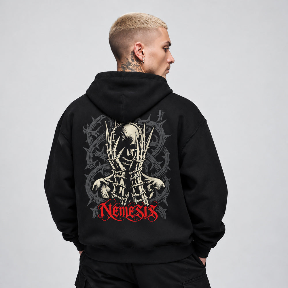 James wearing the black Nemesis hoodie, back view showing an ivory skull framed by long pointed skeletal fingers and barbed wire, with charcoal coils and red Nemesis lettering.