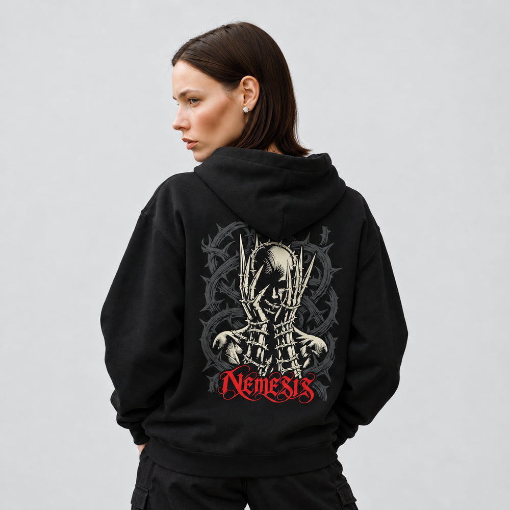 Mara wearing the black Nemesis hoodie, back view showing an ivory skull framed by long pointed skeletal fingers and barbed wire, with charcoal coils and red Nemesis lettering.