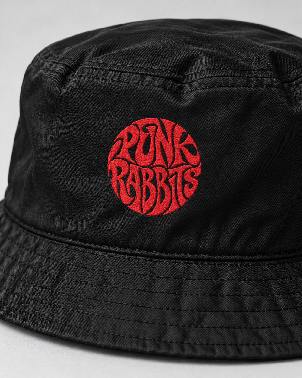 Close-up of red Punk Rabbits embroidery, soft black cotton twill and stitched bucket-hat brim.