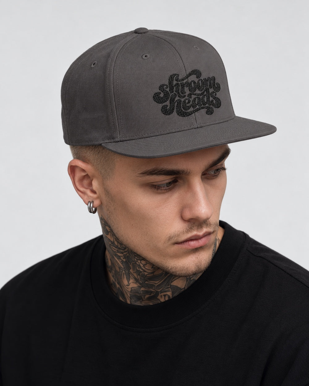 James wearing the Dark Grey Shroom Heads snapback, looking off to the side in a gray studio portrait.