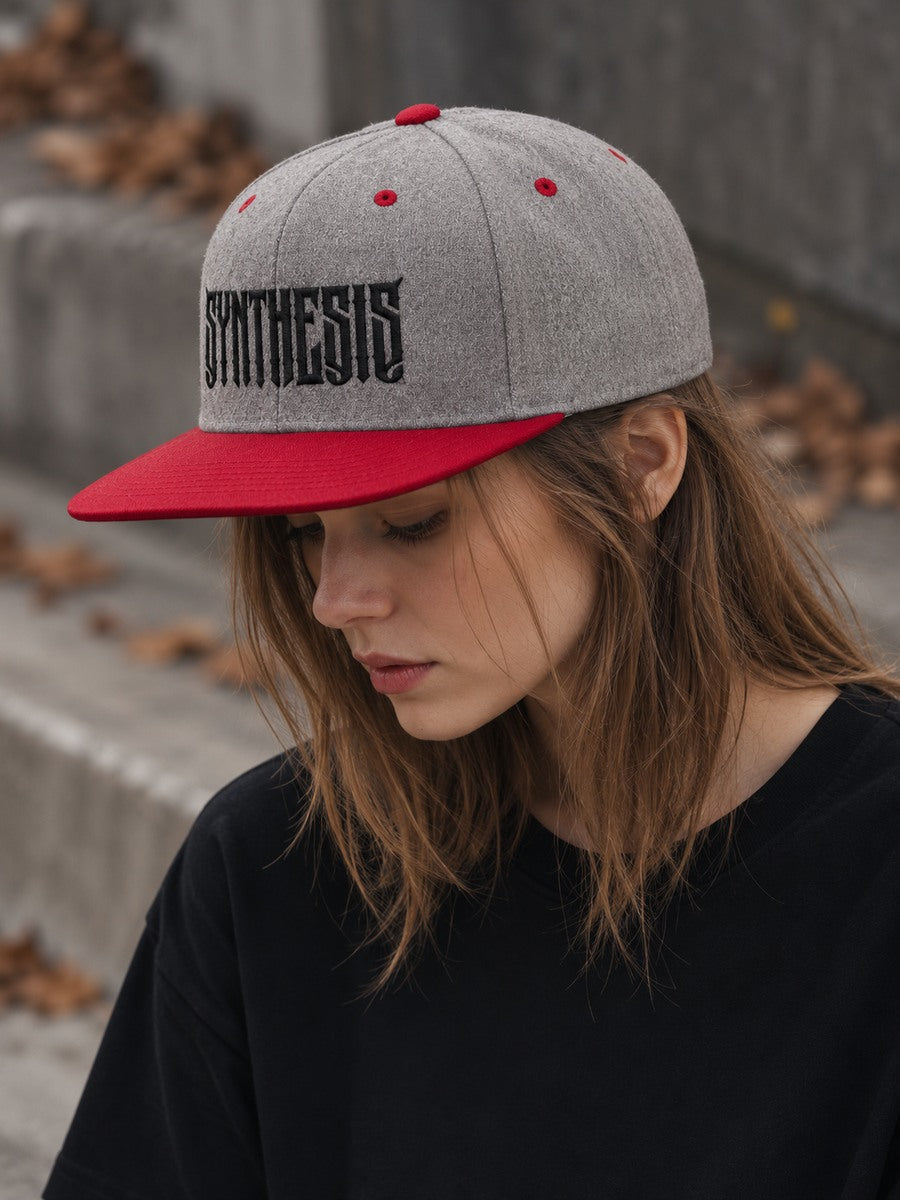 Mara looking down wearing the Synthesis Blackout snapback in Heather Grey and Red, with black angular Synthesis embroidery and full flat bill visible.