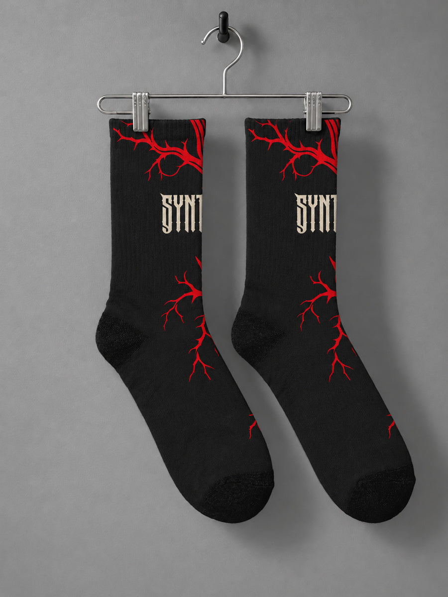 Bleeding Tree Synthesis crew socks, opposite side with sparse red branches and wrapped ivory lettering, hanging as a pair on a metal clip hanger against gray.