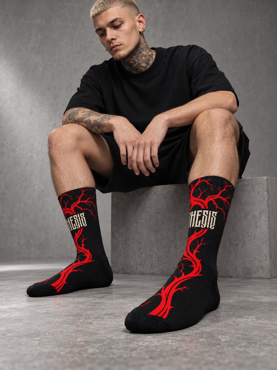 James seated in a gray studio wearing Bleeding Tree Synthesis crew socks, showing the dense red branch side with black toes and heels.