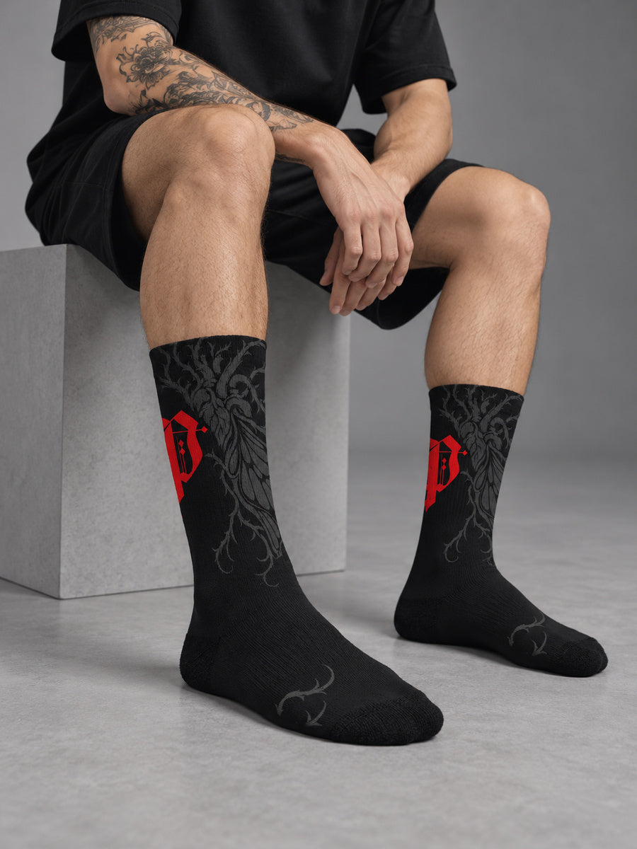 Synthesis Butterfly Roots socks — James wearing the socks, sock-focused studio view, outer patterned view, black with red Gothic P and dark gray butterfly roots.