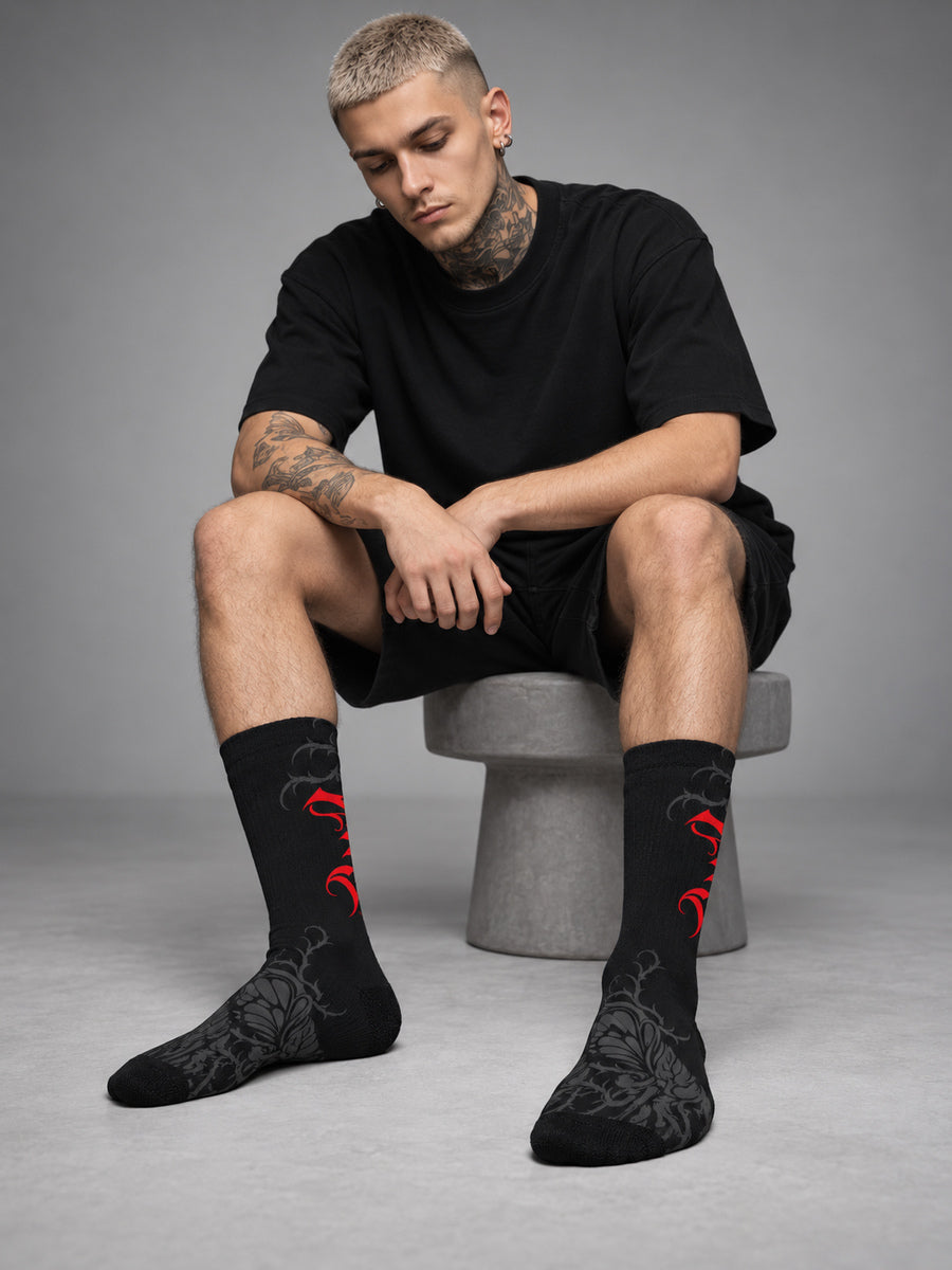 Synthesis Butterfly Roots socks — James wearing the socks, sock-focused studio view, actual printed opposite view, black with red Gothic P and dark gray butterfly roots.