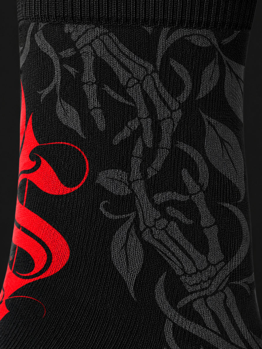 Synthesis Death Grip socks — printed knit macro, outer patterned view, black with red ornate S and dark gray skeletal hands with leaves.