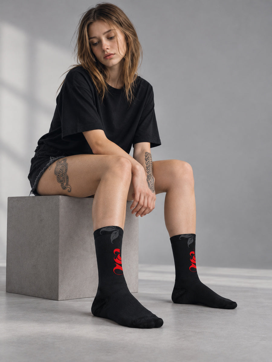 Synthesis Death Grip socks — Mara wearing the socks, sock-focused studio view, actual printed opposite view, black with red ornate S and dark gray skeletal hands with leaves.