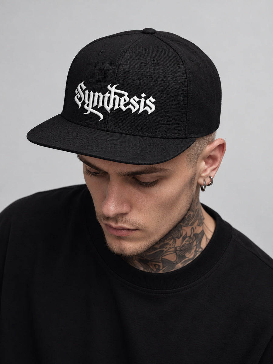 James wearing the black Synthesis Doomed snapback, looking down in a gray studio.