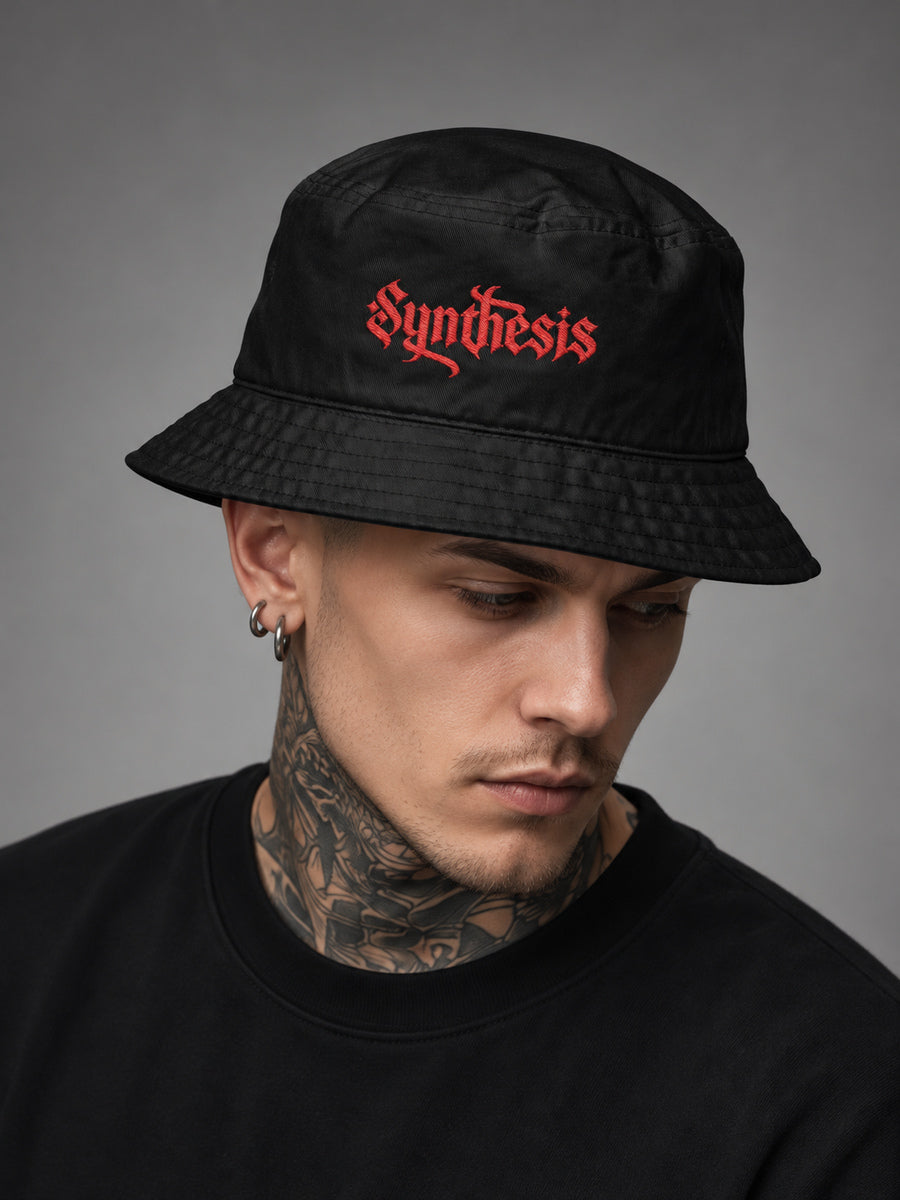 James wearing the black Synthesis Ritual bucket hat with red embroidery, looking down in a gray studio.