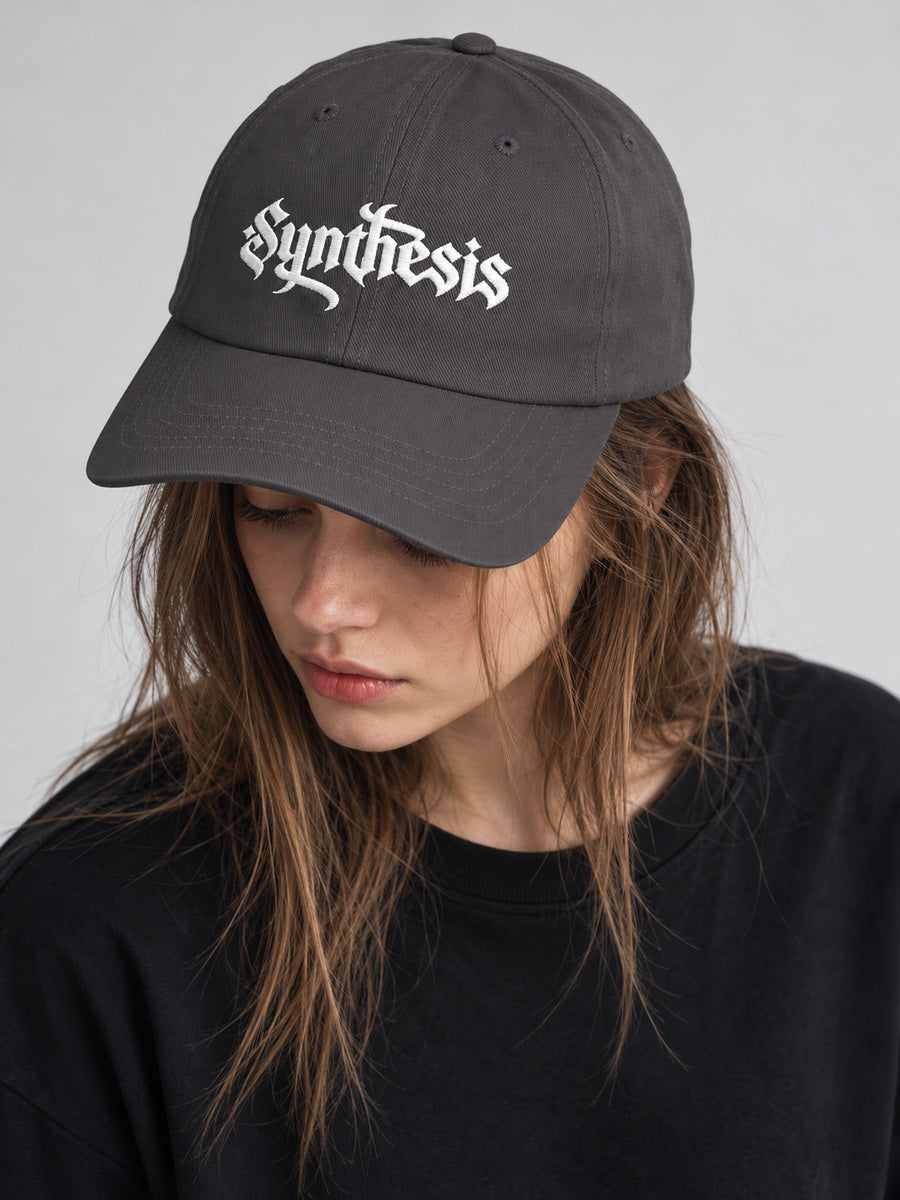 Mara wearing the dark grey Synthesis Ritual cap, candid portrait looking away in the gray studio.