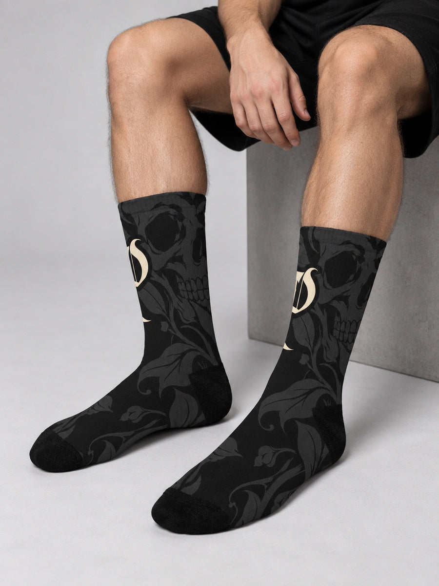 James wearing Synthesis skull bloom socks in a sock-focused seated gray studio view.