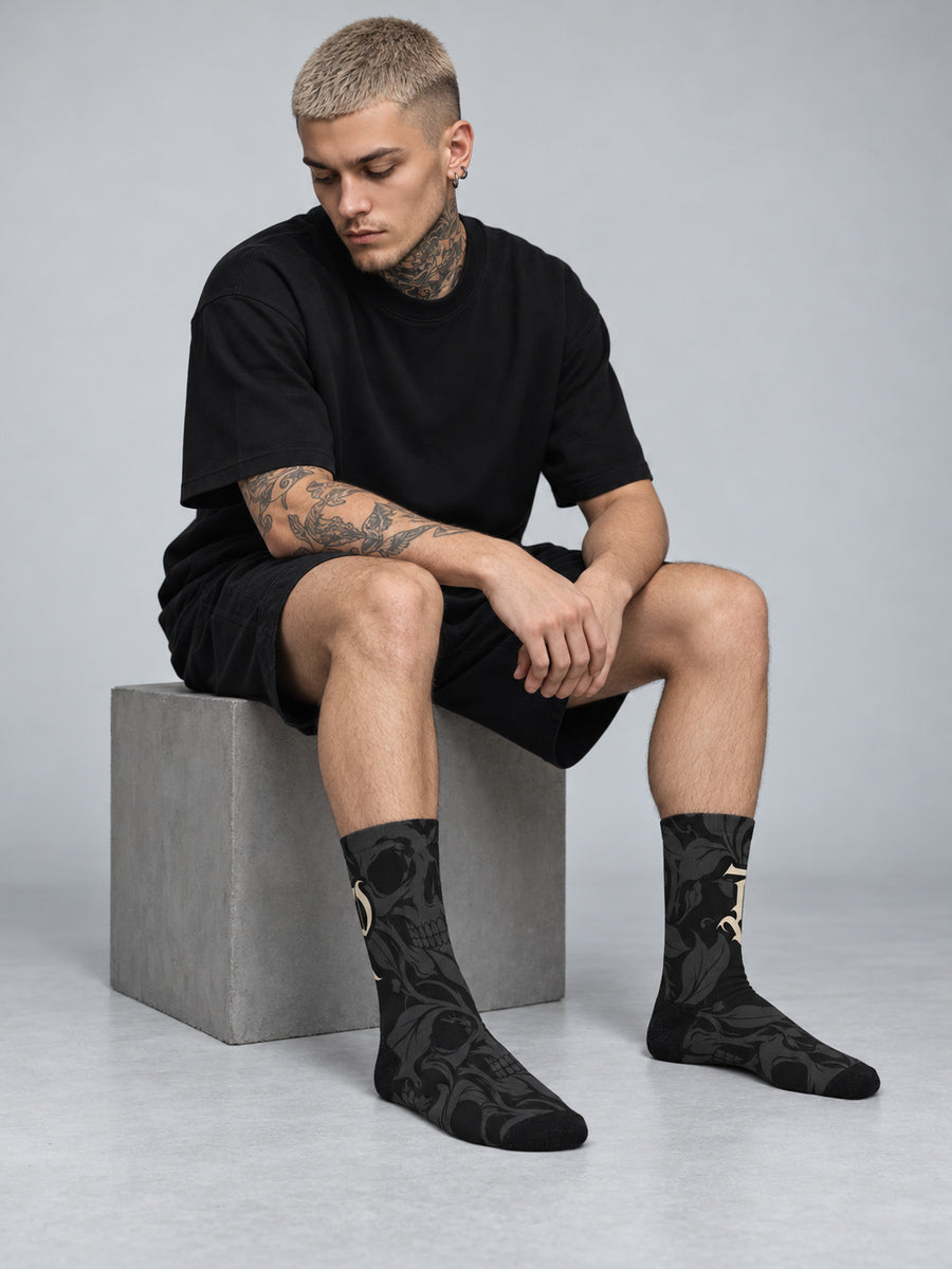 Synthesis skull bloom socks: James seated in the gray studio looking away, complete sock pair visible.