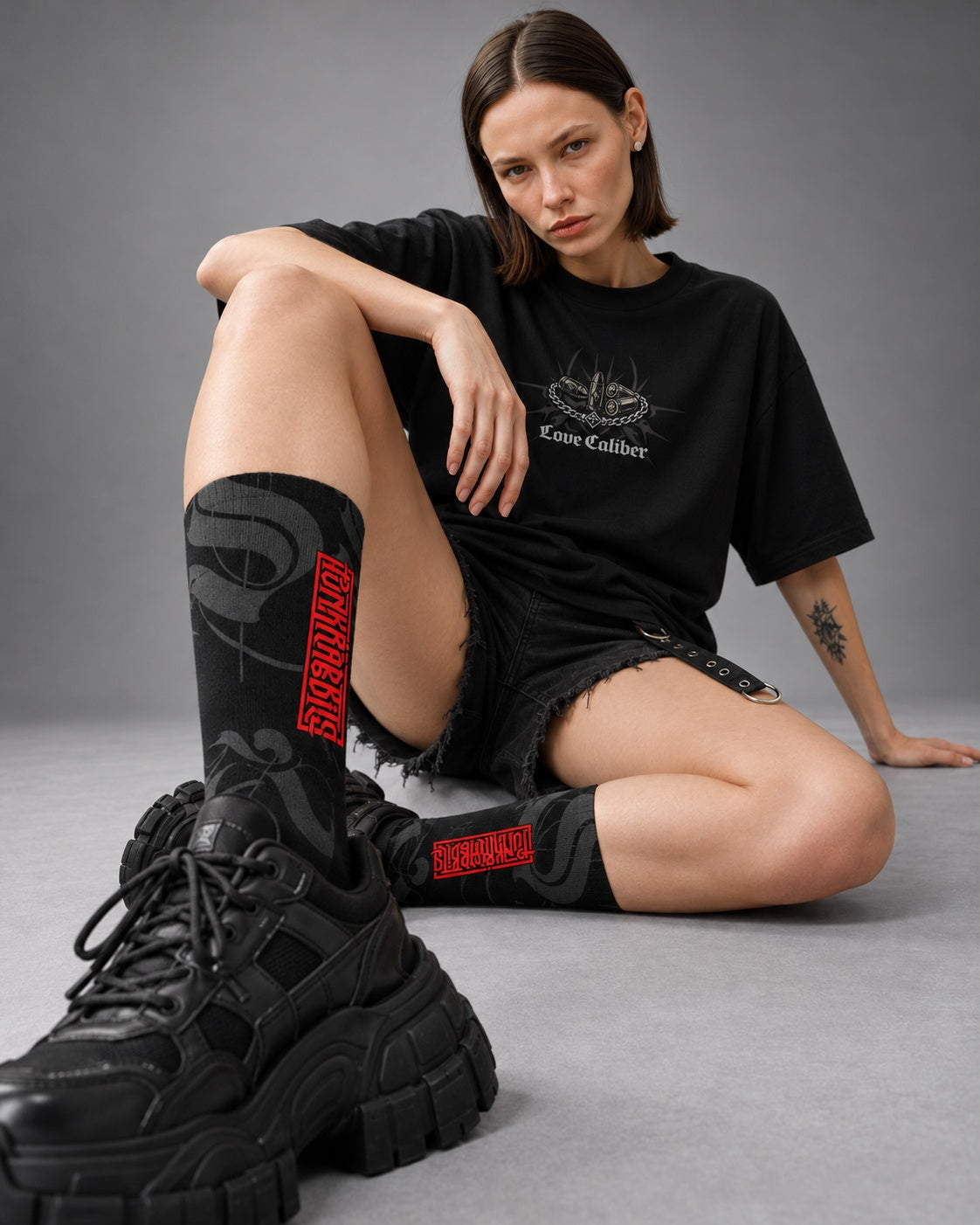 Mara seated wearing black and charcoal Punkrabbits crew socks with red vertical logos and chunky black sneakers