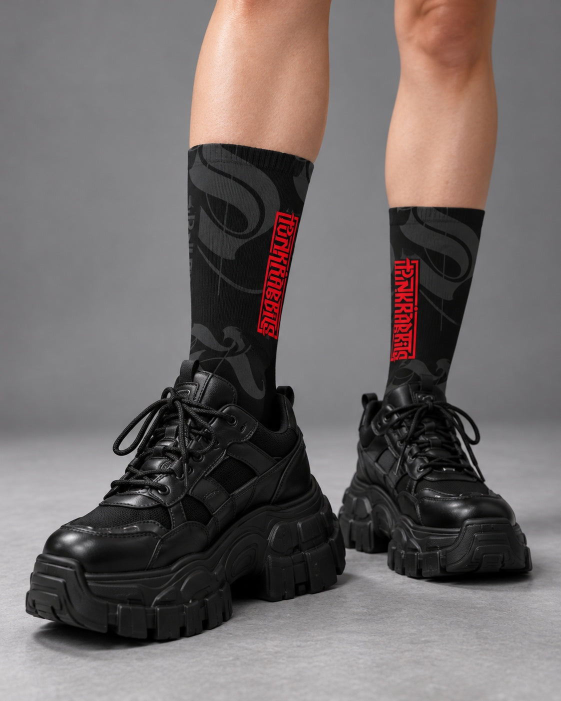 Close-up of black and charcoal Punkrabbits crew socks with red vertical logos styled with chunky black sneakers