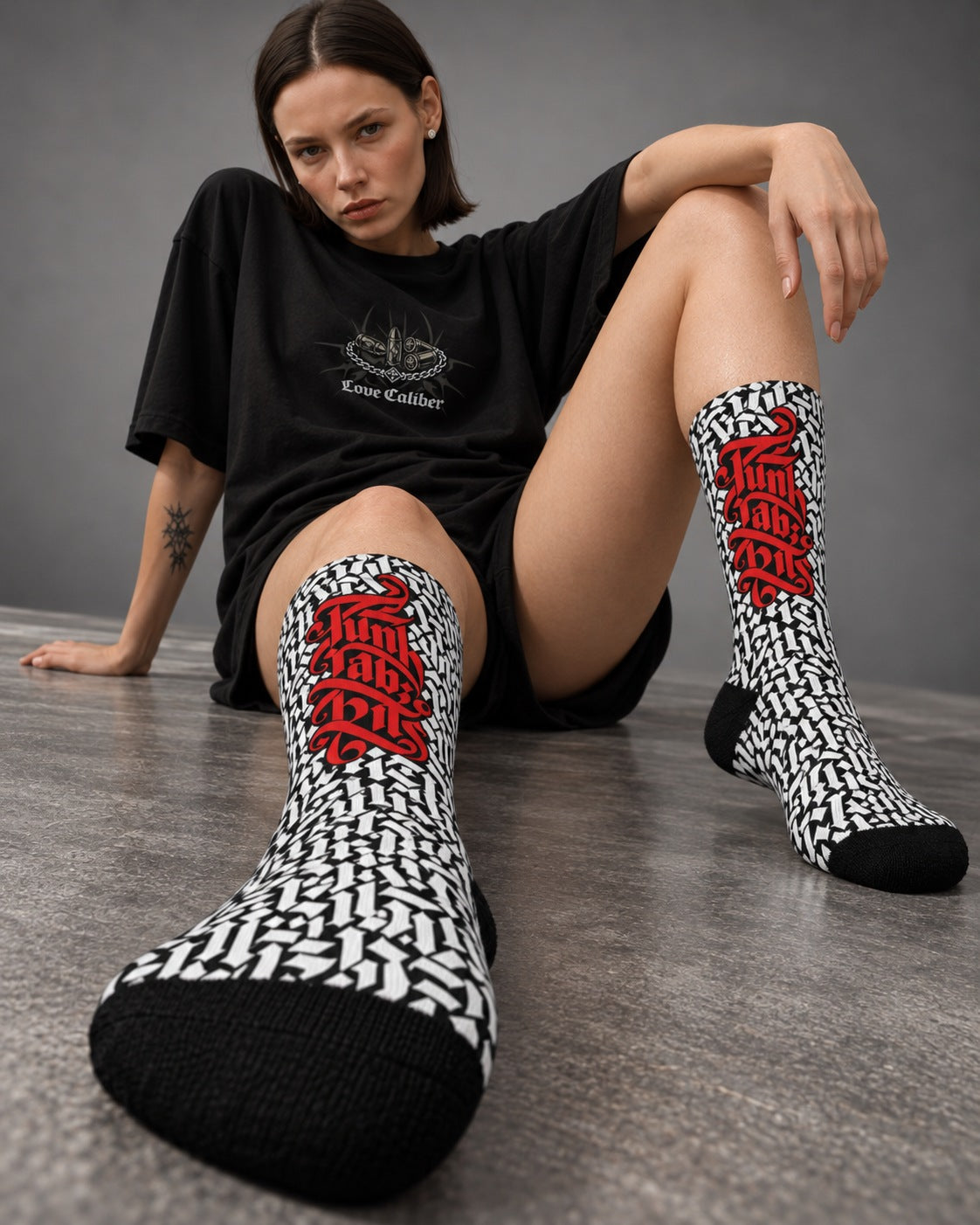 Mara wearing Punkrabbits Red Script crew socks while seated on a grey studio floor