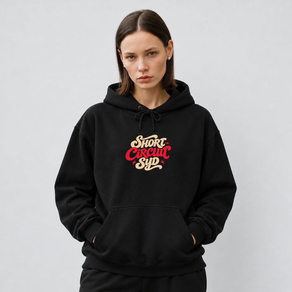 Mara wearing the black Short Circuit Syd hoodie, front view showing stacked cream and red Short Circuit Syd script centered on the chest.