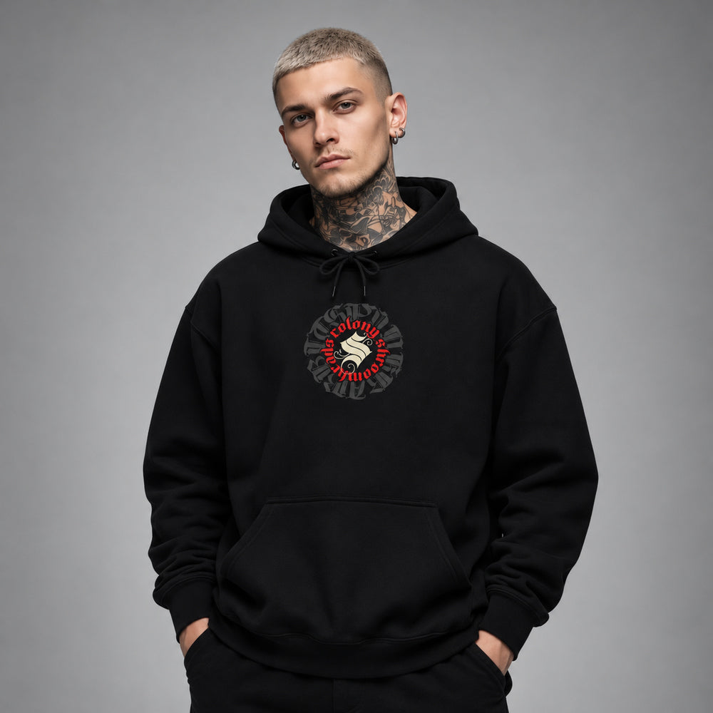 James wearing the black Shroomhead hoodie, front view showing a round Colony Shroomheads crest in red and ivory over charcoal lettering.