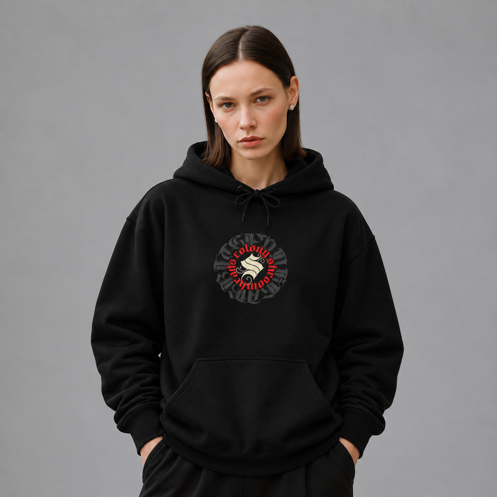 Mara wearing the black Shroomhead hoodie, front view showing a round Colony Shroomheads crest in red and ivory over charcoal lettering.