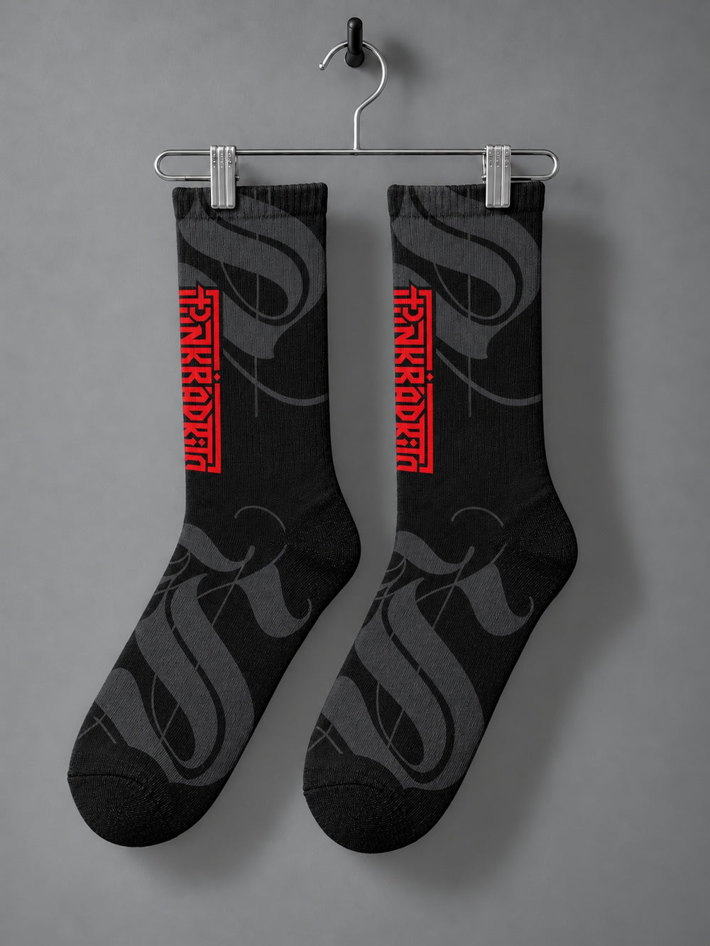 Pair hanging from a chrome clip hanger: black crew socks with charcoal calligraphic strokes and a vertical red Punkrabbits wordmark.