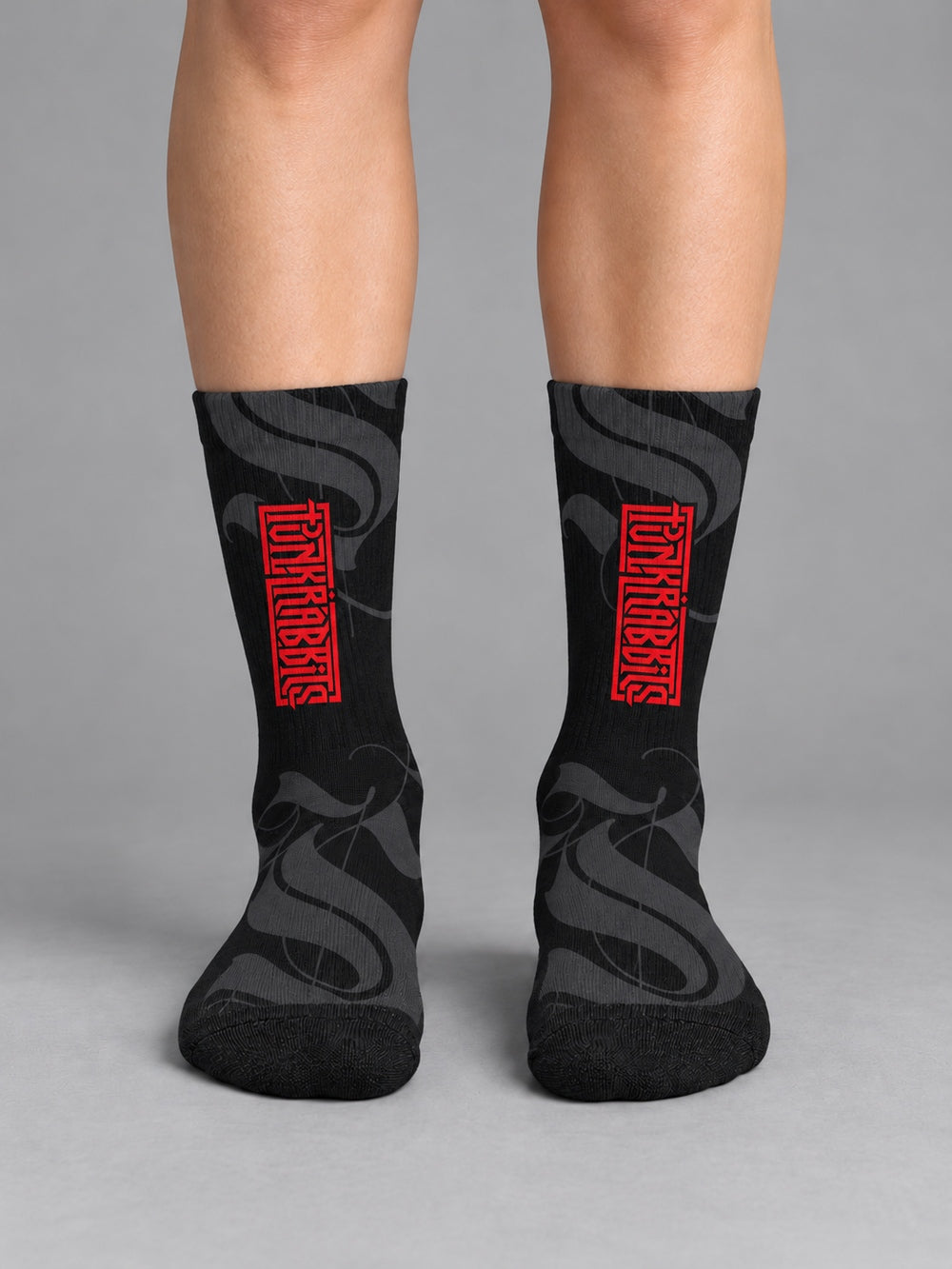 Front view worn on lower legs without shoes: black crew socks with charcoal calligraphic strokes and a vertical red Punkrabbits wordmark.
