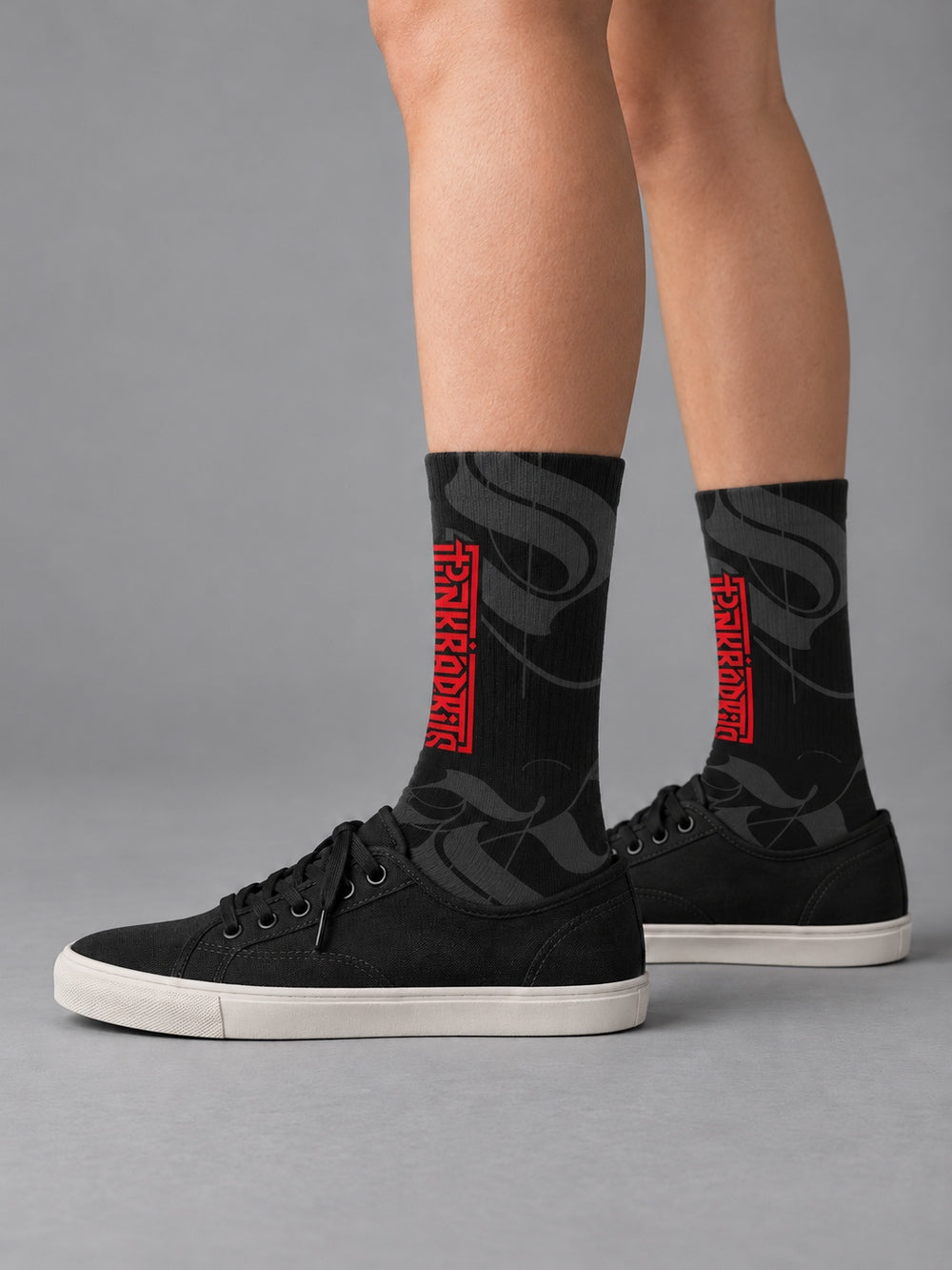 Side view worn with black low-top canvas shoes: black crew socks with charcoal calligraphic strokes and a vertical red Punkrabbits wordmark.