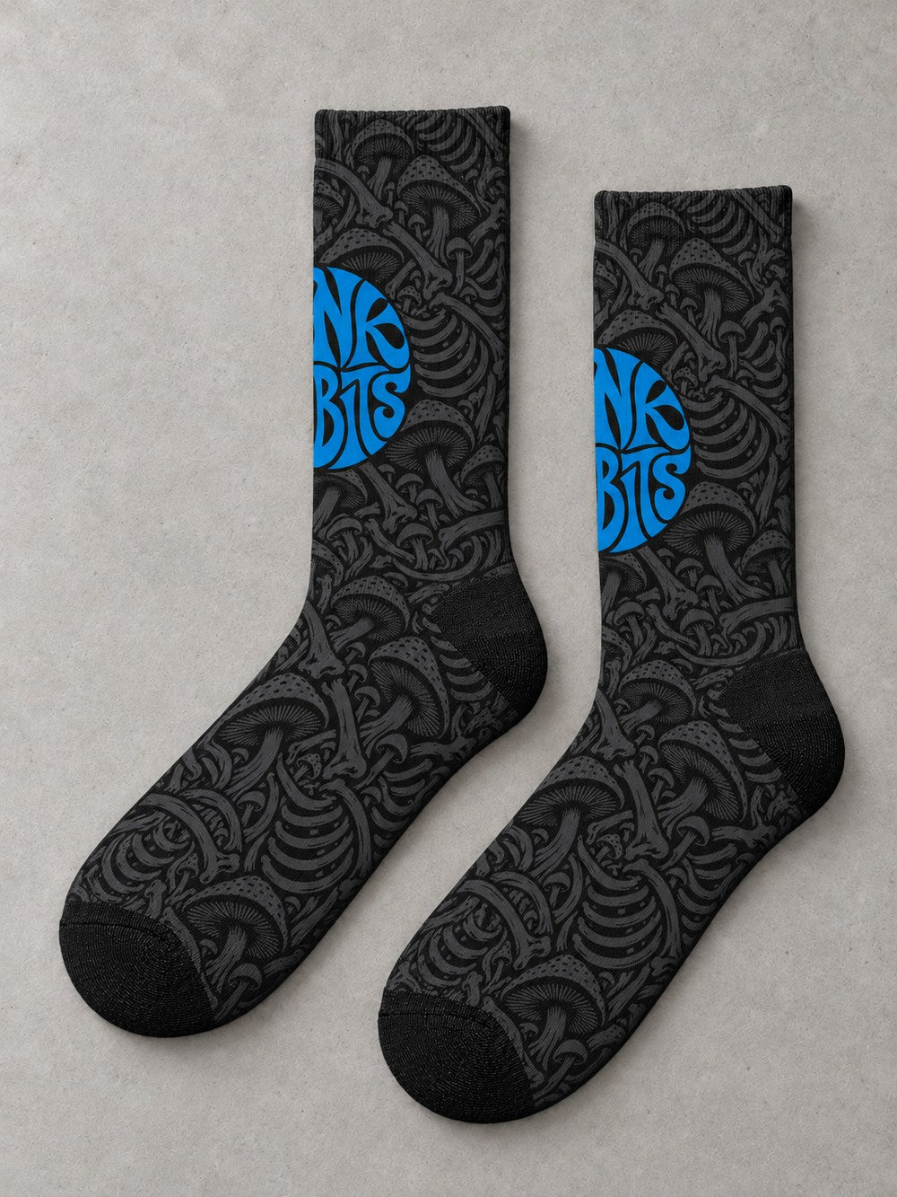 Overhead flat-lay pair in side profile: black crew socks with charcoal mushroom and skeletal artwork and a blue circular Punkrabbits logo.