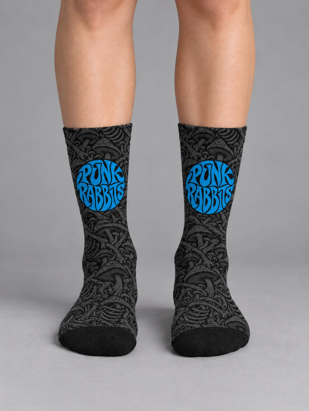Front view worn on lower legs without shoes: black crew socks with charcoal mushroom and skeletal artwork and a blue circular Punkrabbits logo.