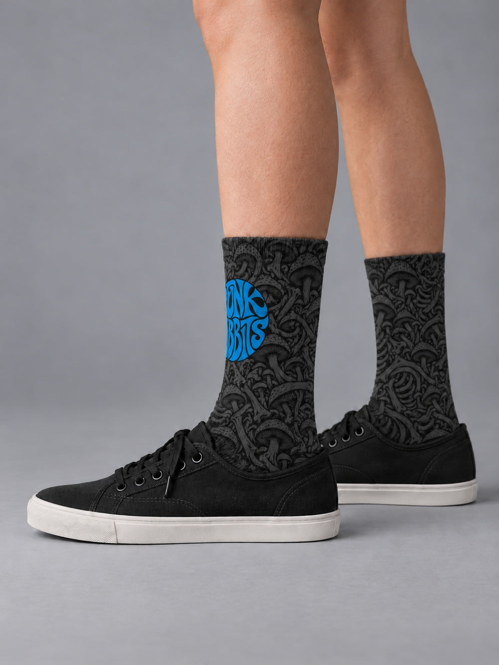 Side view worn with black low-top canvas shoes: black crew socks with charcoal mushroom and skeletal artwork and a blue circular Punkrabbits logo.
