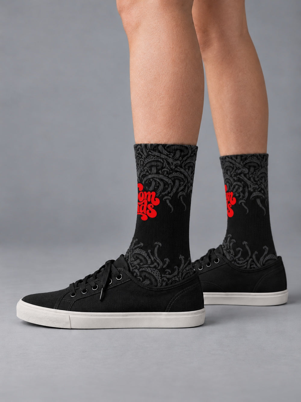 Side view worn with black low-top canvas shoes: black crew socks with fading charcoal mushroom artwork and red Shroomheads script.