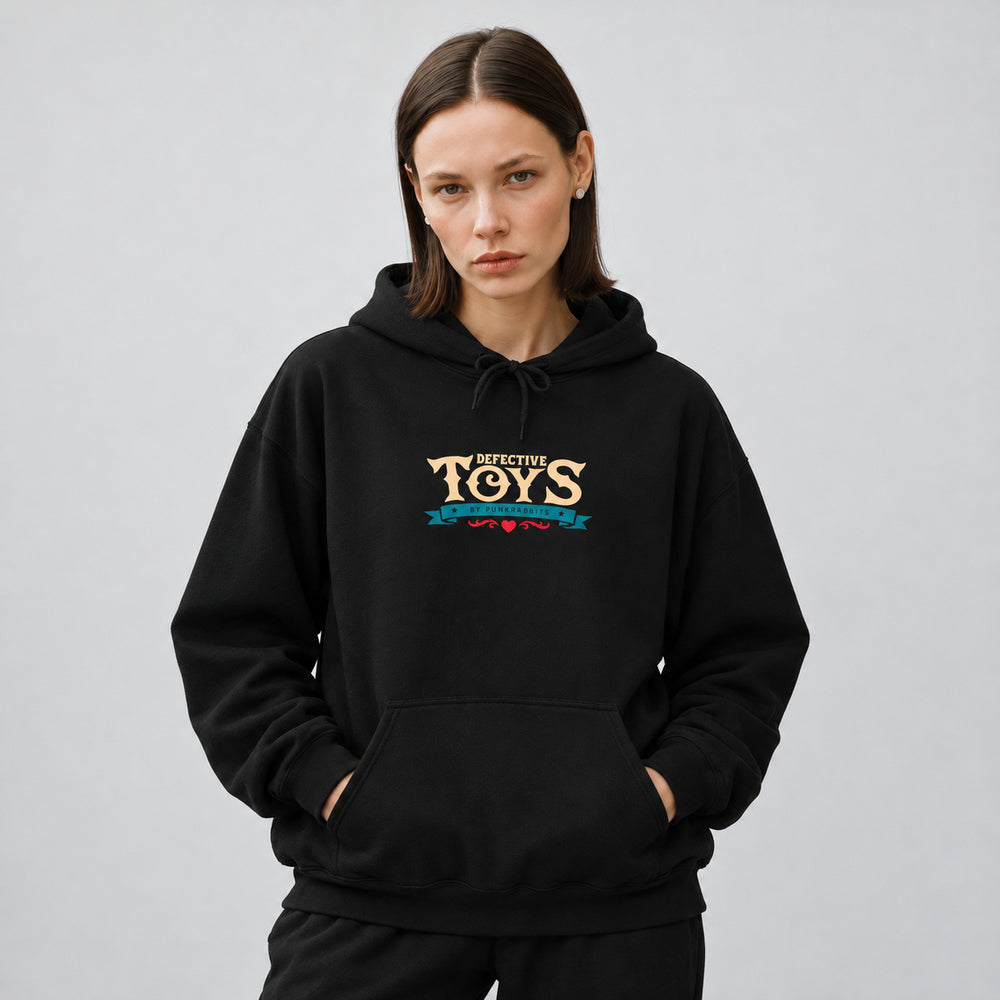 Mara wearing the black Sinister Sussie hoodie, front view showing cream Defective Toys lettering above a teal Punkrabbits banner and a small red flourish.