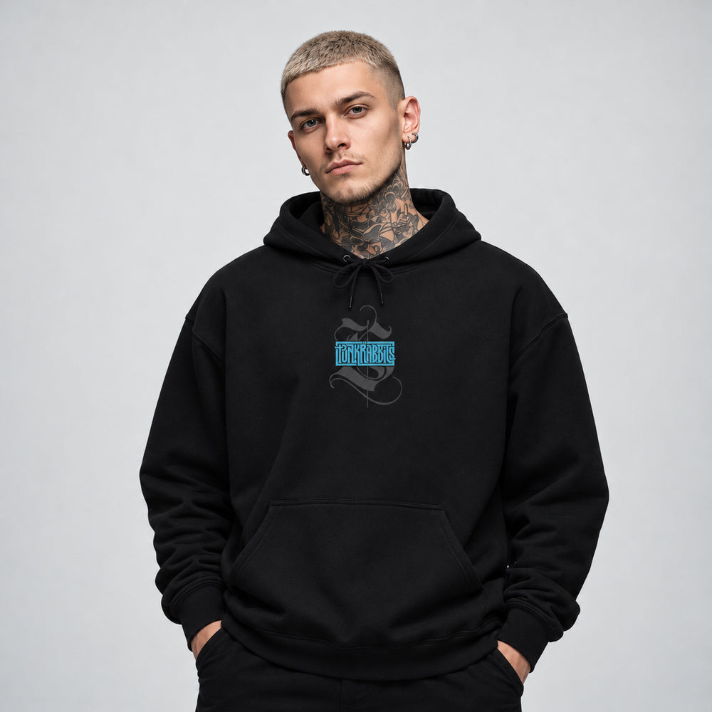 James wearing the black Spore Keeper hoodie, front view showing a compact blue Punkrabbits wordmark over a charcoal calligraphic motif.